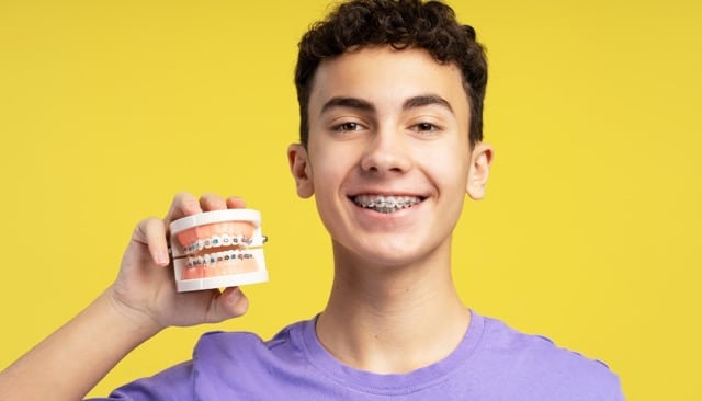 Teen boy smiling with braces and orthodontic model in hand