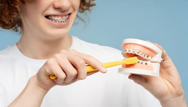 Teen brushing teeth model with braces to demonstrate proper technique
